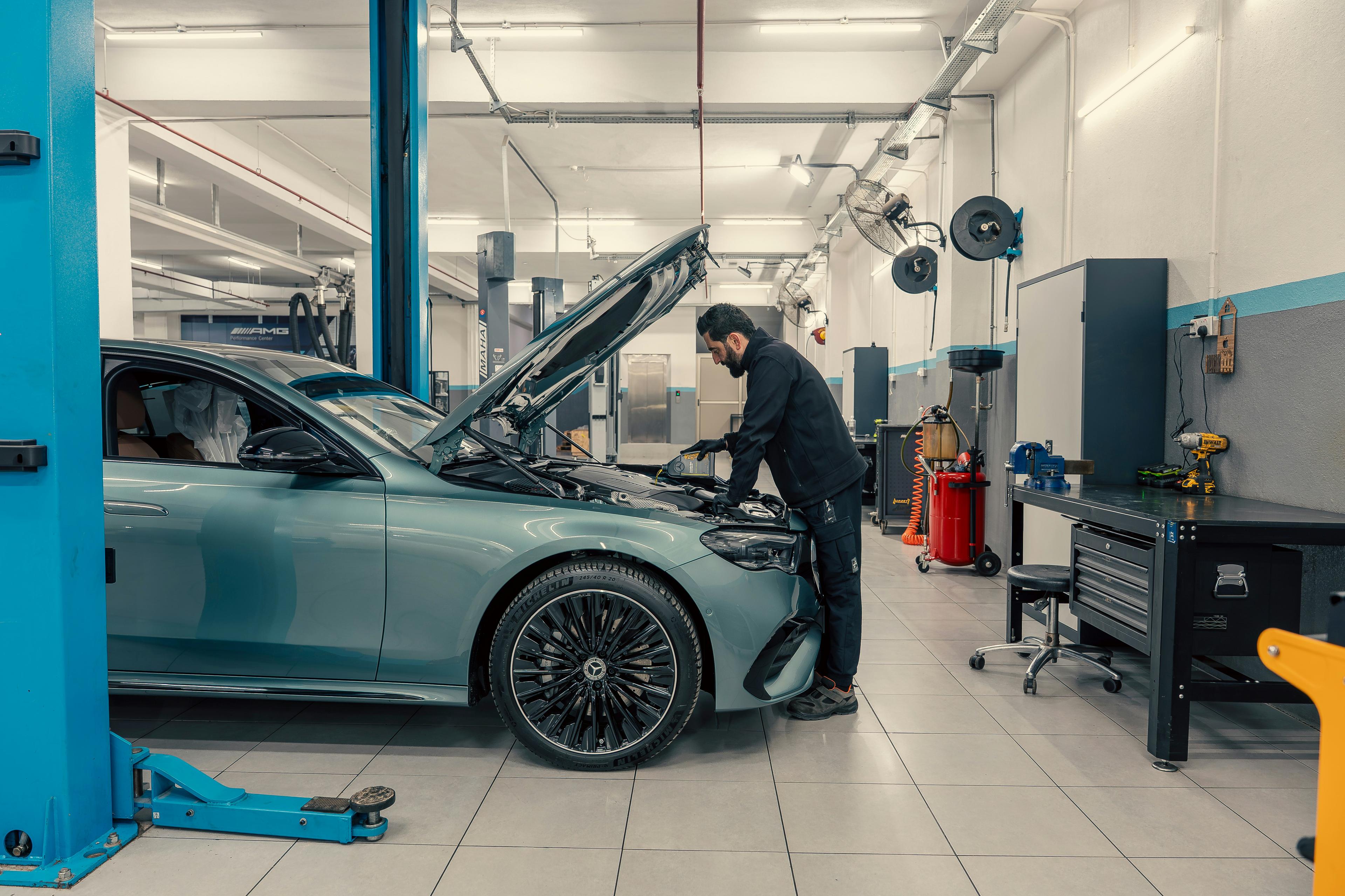Mechanic working under the bonnet of a car in a bright, tidy workshop